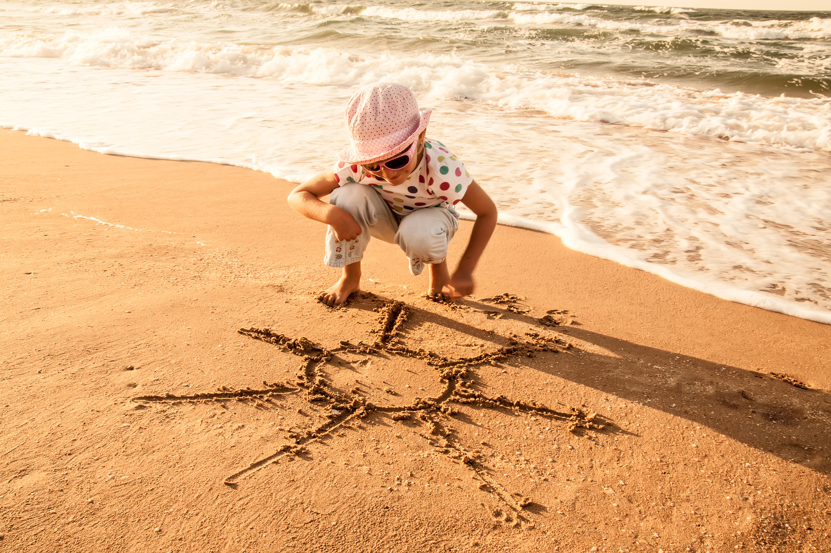 little girl draws  sun on sand at the beach